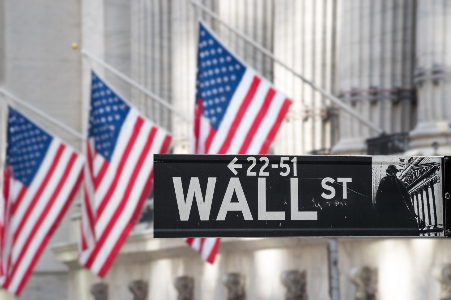 Wall Street, the front of the New York Stock Exchange, and American flags