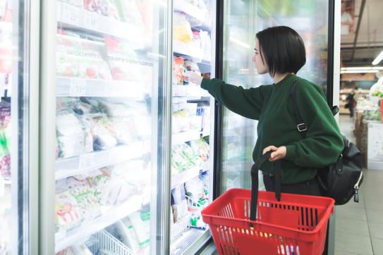 A supermarket shopper opens a freezer to pull out some frozen food
